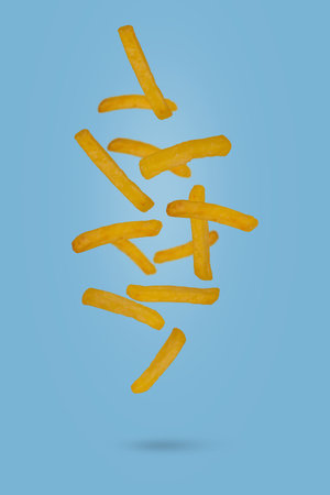 French fries - fried potatoes flying in air. Fast food levitating on blue background. Creative food...