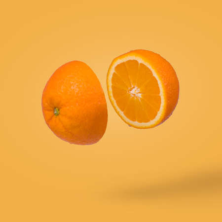 Minimal idea with juicy orange cut in two halves flying in the air. Summer citrus fruit refreshment. Vitamins, fresh healthy food concept.の写真素材