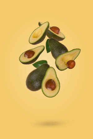 Fresh whole and sliced avocado flying in air isolated on pastel yellow background. Healthy food, diet, tropical exotic fruit, trendy food product. Creative and minimal food concept.の写真素材
