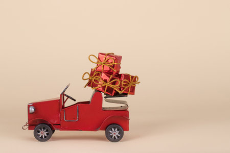 Old red car carrying Christmas or New Year  gifts isolated on a beige background. Creative minimal  Holiday concept.の写真素材