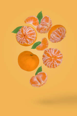 Fresh ripe whole and sliced mandarine flying in air isolated on a yellow background. Vitamins, diet, healthy food concept.の写真素材