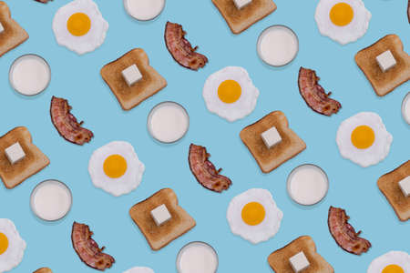 Pattern made with fried eggs, slices of crispy bacon, toast bread and glasses of milk on pastel blue background. Minimal and creative breakfast concept. Top view. Flat lay.の写真素材