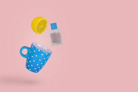 Creative concept with tea cup, flying tea bag and lemon slice isolated on pink background. Minimal...