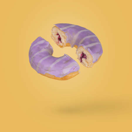 Donut with blueberries cut into two parts flying on yellow background. Minimal dessert and sweet conceptの写真素材
