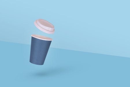 One disposable paper coffee cup with white cap flying in air isolated on blue background. Minimal...