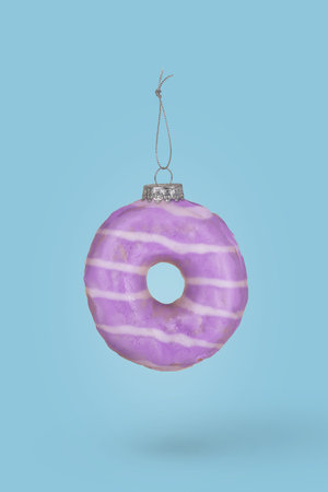 Christmas bauble decoration made of pastel purple doughnut on blue background. Minimal holiday and New Year concept.の写真素材