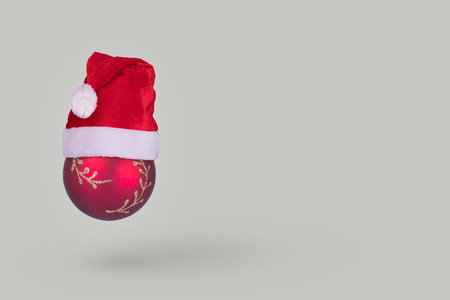 Red Christmas bauble ball ornament with Santa Claus hat flying in air isolated on gray background....