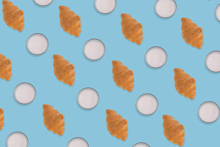 Creative pattern made of freshly baked croissant and glass of milk on pastel blue background. Minimal homemade pastry concept.の写真素材