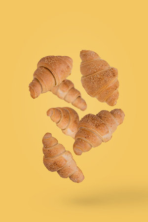 Freshly baked croissants fly in the air isolated on a yellow background. Creative breakfast food concept.の写真素材