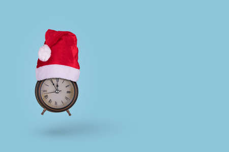 Vintage alarm clock in a Santa Claus hat flying in air  on a blue background. Winter season and Minimal Christmas time concept.の写真素材