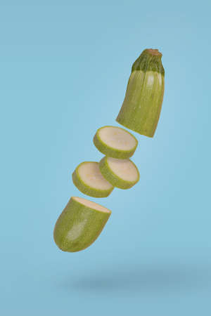 Fresh organic zucchini, sliced into rings floats freely in the air against blue background. Creative concept of fresh vegetables, diet, flying food.の写真素材