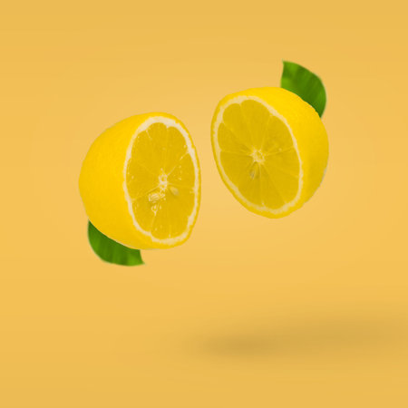 Juicy lemon cut in two halves flying in the air on a bright yellow background. Summer citrus fruit refreshment. Vitamins, fresh healthy food concept. Minimal fruit idea.の写真素材