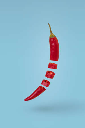 Sliced red hot chili pepper floating in air isolated on blue background. Minimal food concept.の写真素材