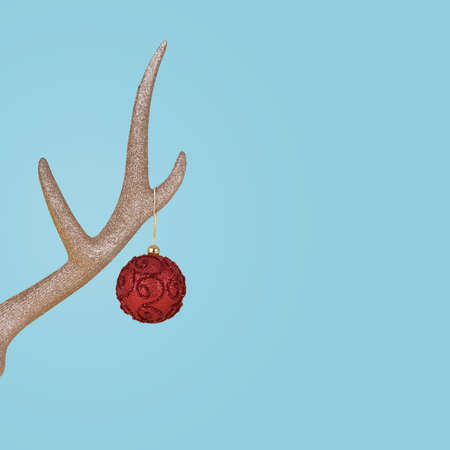 Golden reindeer antler with red Christmas bauble ball on pastel blue background. New Year minimal concept.の写真素材