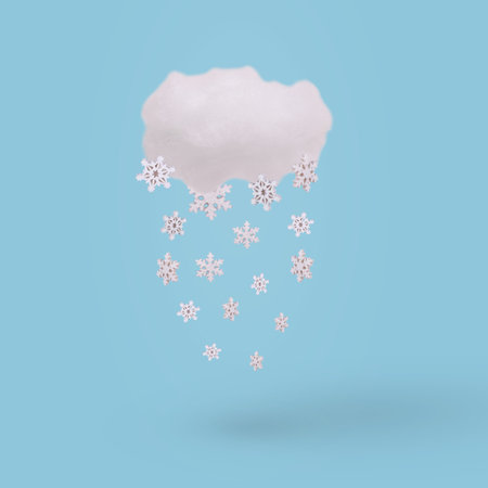 Creative concept with cloud and falling winter snowflake on bright blue background. Minimal winter...