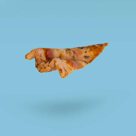 Pizza slice flying in air isolated on a bright blue background. Creative food delivery concept. Restaurant or pizzeria banner.の写真素材