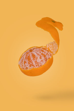 Creative food concept with fresh ripe peeled mandarin flying in air isolated on a yellow background. Vitamins, diet, healthy food concept.の写真素材