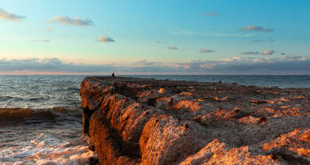Beautiful sunset on the Baltic Sea with an old concrete pier in the background lit by the rays of the setting sun, the sky in various shades of blue, partly with clouds, romantic moodの写真素材