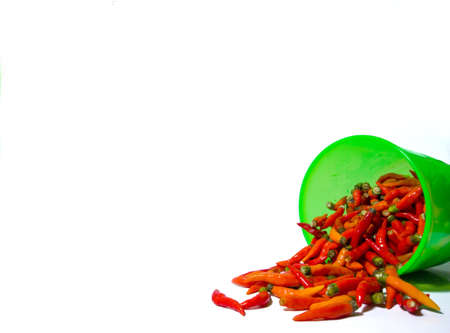 Some red chilies are in a green jar placed in a jar with spilled on white paper and isolated on a white background. red chili isolated on a white backgroundの写真素材