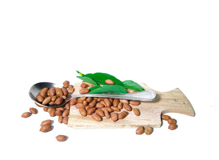 peanuts and stainless spoon flat lay on a wooden cutting board . isolated on a white background....