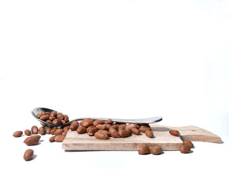 Peanuts and stainless spoon lay on a wooden cutting board . isolated on a white background. food ingredients in the form of nuts in the kitchenの写真素材