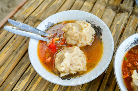 the delicious Two Mie Pentol Bakso or meatball soup in the white bowl with spoon and fork. Two...