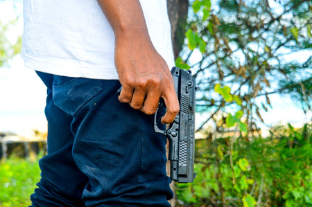Man carrying a gun in his hand and ready to shooting. Concept of man terrorist, killer, armed forces, soldier,Theft, criminals, Crime of violence. focus on gun, noisy, exposure, similar othersの写真素材