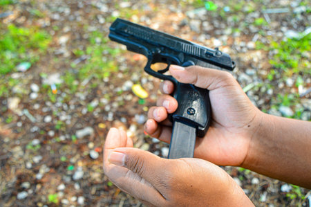 A man hand holds a gun and is preparing bullets for reloading. Concept of man terrorist, killer, armed forces,Theft, criminals, Crime of violence. focus on gun, noisy, exposure, similar othersの写真素材