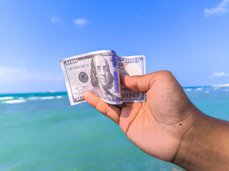 Hand holding 100 dollar bill in hand, financial concept, vacation, tax, success, salary. Summer sea...