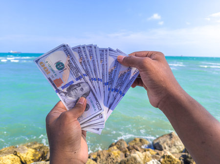 Hand holding 100 dollar bill in hand, financial concept, vacation, tax, success, salary. Summer sea...