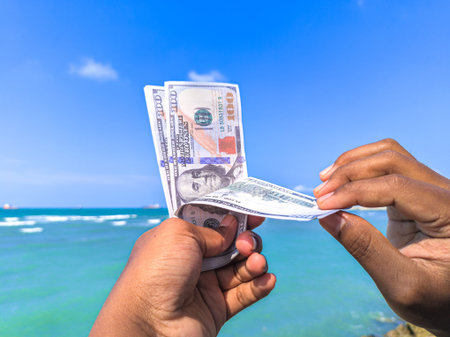 Hand holding 100 dollar bill in hand, financial concept, vacation, tax, success, salary. Summer sea...