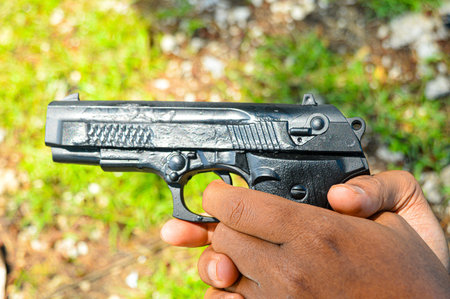 Closep up of The hand of a security man, policeman, terrorist, thief, is carrying a gun and ready to shoot. Crime concept, Military, crime shooting. focus on gun, noisy, exposure, similar othersの写真素材