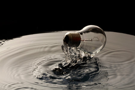 Light bulb falling into water, isolated on black background. Concept of ideaの写真素材