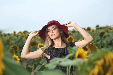 Happy young woman walking in blooming sunflower field throwing hat up and having fun.の写真素材
