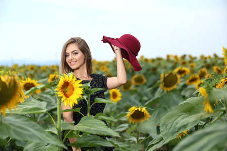 Happy young woman walking in blooming sunflower field throwing hat up and having fun.の写真素材