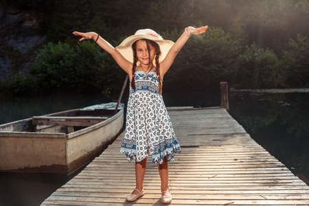 Beautiful little girl in a colorful dress with a hat on her head enjoys the summer dayの写真素材
