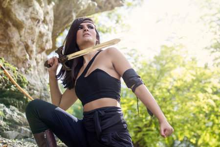 Beautiful warrior girl with sword in hand hidden among rocks - warrior woman conceptの写真素材