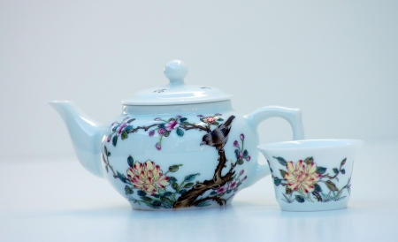 Tiny white teapot and cup is a unique design painted on the glassware.  This is set against a white background.の写真素材