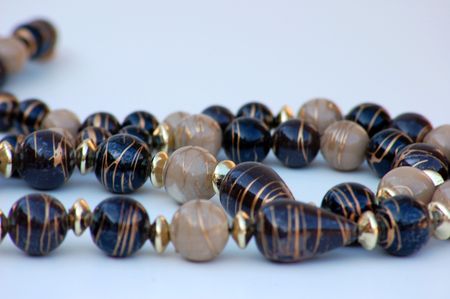 Macro shot of white and dark brown beaded necklace with gold swirls against a white background.の写真素材