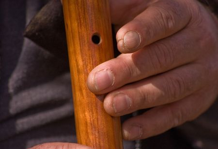 A closeup shot of a man's rough labor working hands, playing a wooden Native American flute.の写真素材