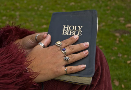 Closeup of a woman's hand with many rings on a worn black Holy Bible.  Darker skin hand wearing...