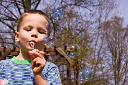 This young 4 year old boy is having a great time blowing bubbles outdoors.