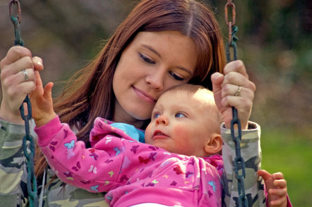 This young mom and baby daughter are enjoying a moment of cuddling and snuggling on a swing for a...