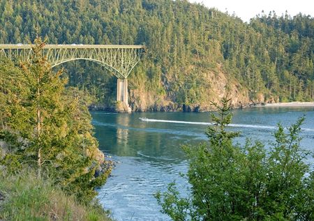 This speed boat is quickly going under a beautiful bridge setting at Deception Pass Washington.の写真素材