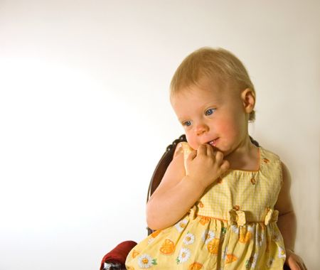 Photo of a sweet little 1 year old Caucasian girl with blond hair sitting on a chair with a shy, coy facial expression.の写真素材