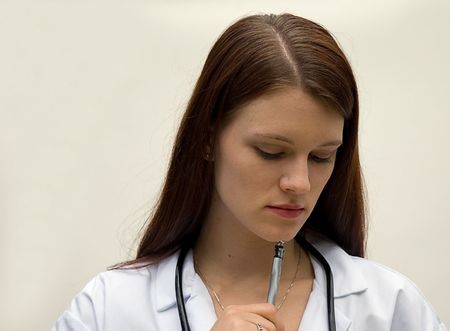 This young brunette Caucasian woman represents a medical doctor, deep in thought with pen and stethoscopes around neck.の写真素材
