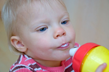 This cute toddler girl with blond hair is drinking milk from a sippie cup for healthy growth.