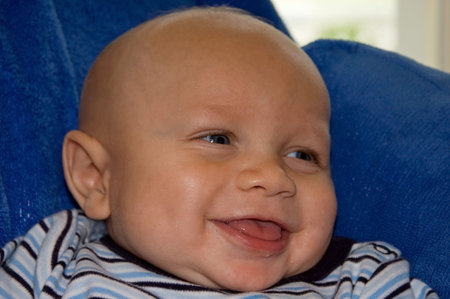 This cute bi-racial baby boy is smiling and happy.  He's sitting against a blue blanket.