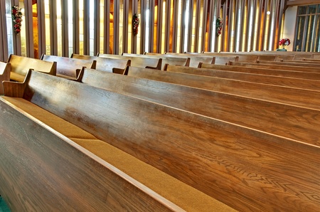 This stock image has rows of empty wooden church pews with sunlight filtering through the vertical stained glass windows.のeditorial素材