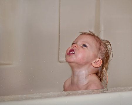 This toddler girl with red hair is sitting in a bathtub and is looking up with a humorous facial...